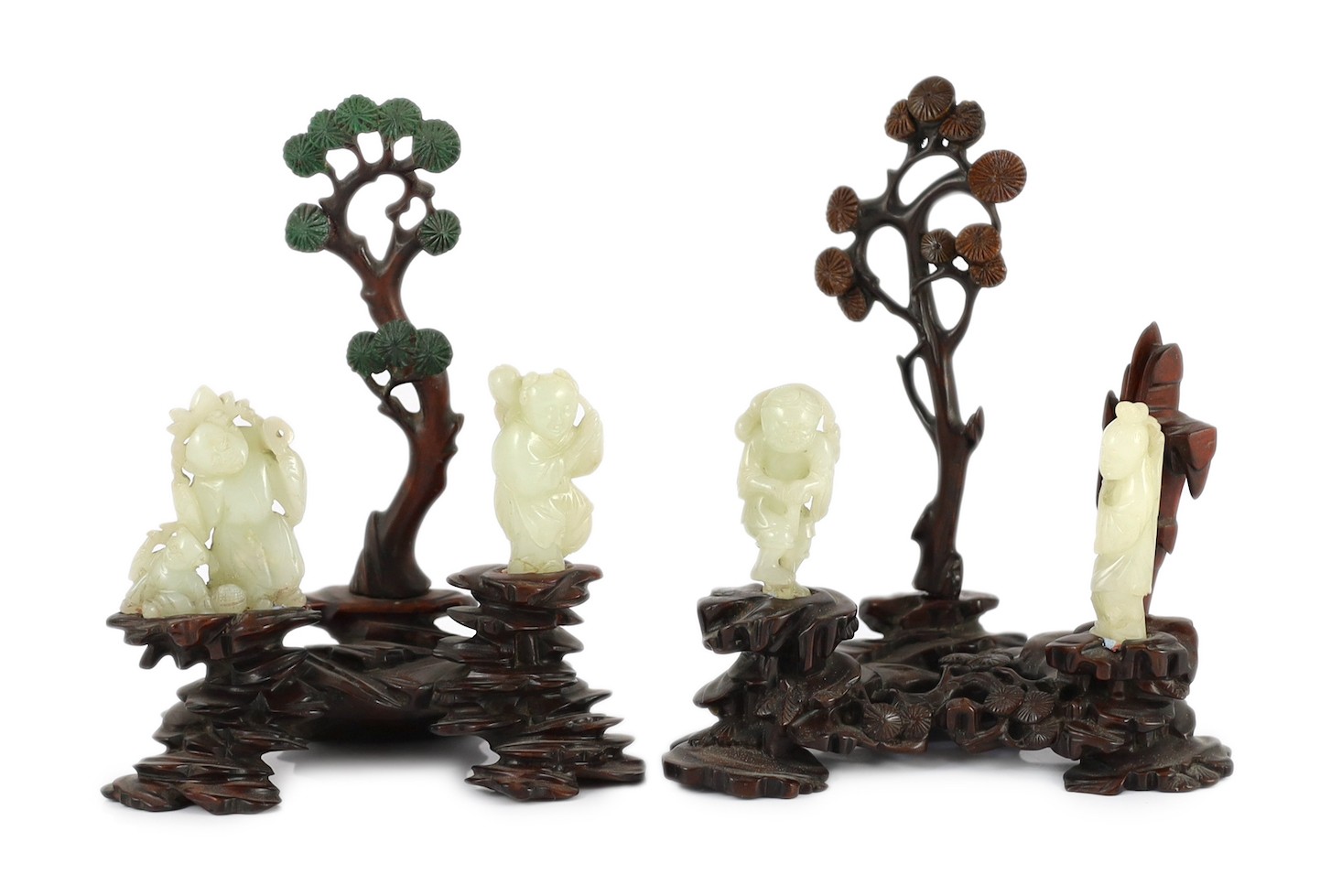 An assembled group of four Chinese pale celadon jade figures, 18th/19th century, displayed on two later wood 'rock-work' stands, total height approximately 19cm high